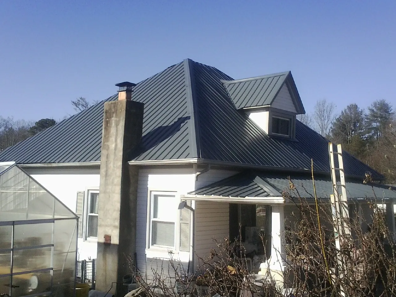 Dark blue standing seam metal roof on a white farmhouse with dormer — Slate & Tile Roof Repair by Roofing Brothers in Halls