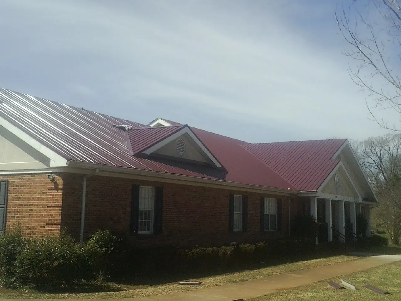 Red metal roof with gabled entries on a long brick building, from a Hail Damage Roof Repair job in Halls