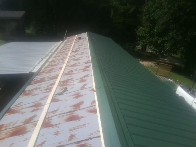 Old rusted panels beside newly installed green metal roofing — Wind Damage Roof Repair by Roofing Brothers in Halls