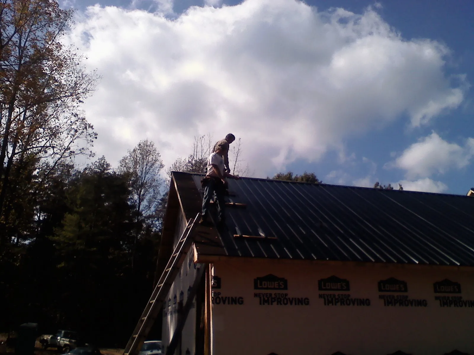 Roofer fastening dark metal panels high against a cloudy sky, from a Roof Inspection job in Halls